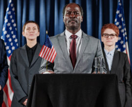 Schwarzer männlicher Politiker und Mitarbeiter schütteln Hände vor blitzenden Kameras