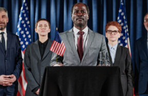 Schwarzer männlicher Politiker und Mitarbeiter schütteln Hände vor blitzenden Kameras